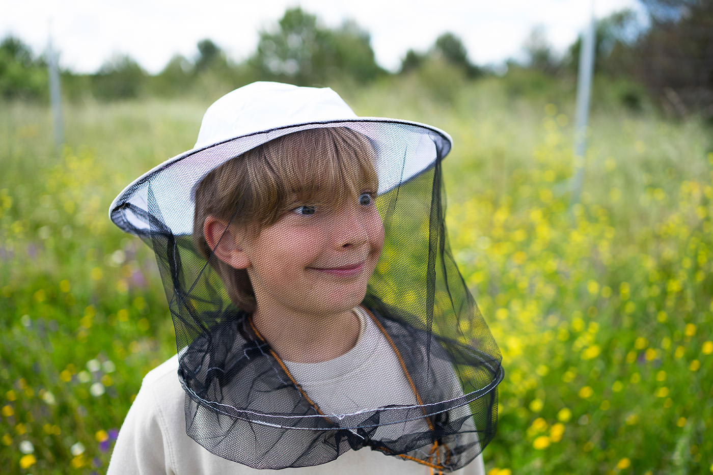 Young boy smiling in beekeeping outfit in meadow with a funny face Boy wearing beekeeping gear standing in a vibrant wildflower field